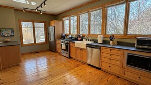 A kitchen with wooden cabinets, a stainless steel refrigerator, a dishwasher, a stove, and a large window with a view of trees. - Large home Assoc Beach across street Firepit Scrnd Porches (Union Pier)