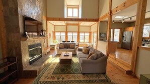 A spacious living room with a fireplace, a sofa set, and a dining area. - Large home Assoc Beach across street Firepit Scrnd Porches (Union Pier)