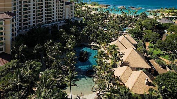 Ein Resort mit einem großen Gebäude, einem Schwimmbecken und einem Strand mit Palmen.