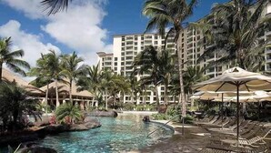 Ein Poolbereich eines Resorts mit Liegestühlen und Sonnenschirmen, umgeben von Palmen und einem großen Gebäude im Hintergrund.