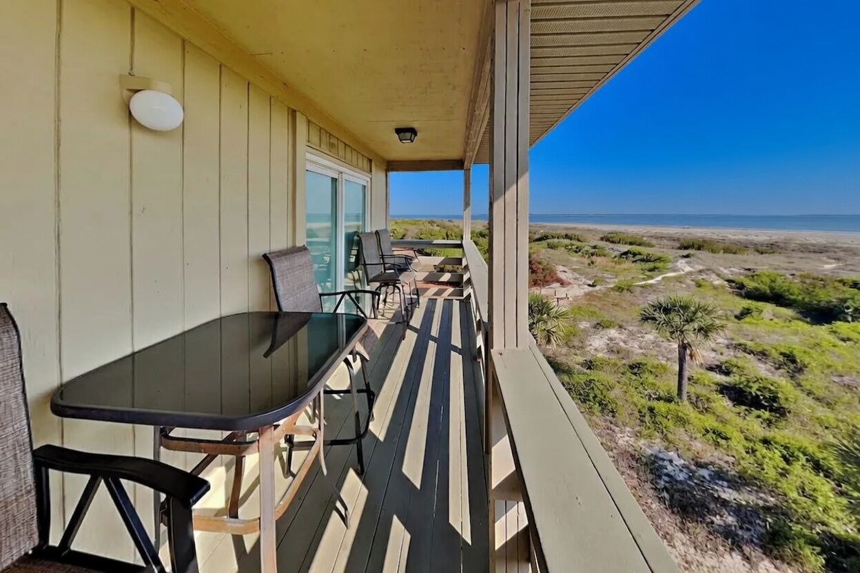 Un espace extérieur abrité, doté d’une table et de chaises, offrant une vue sur la plage et comprenant une terrasse en bois.