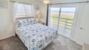Een slaapkamer met een bed, plafondventilator, raam met gordijnen, nachtkastje en uitzicht op de omgeving.