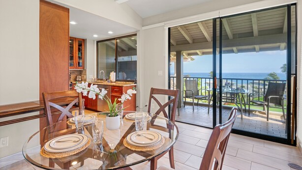 Un espace repas avec une table en verre, des chaises et une vue sur l’océan, accessible par une porte-fenêtre coulissante.