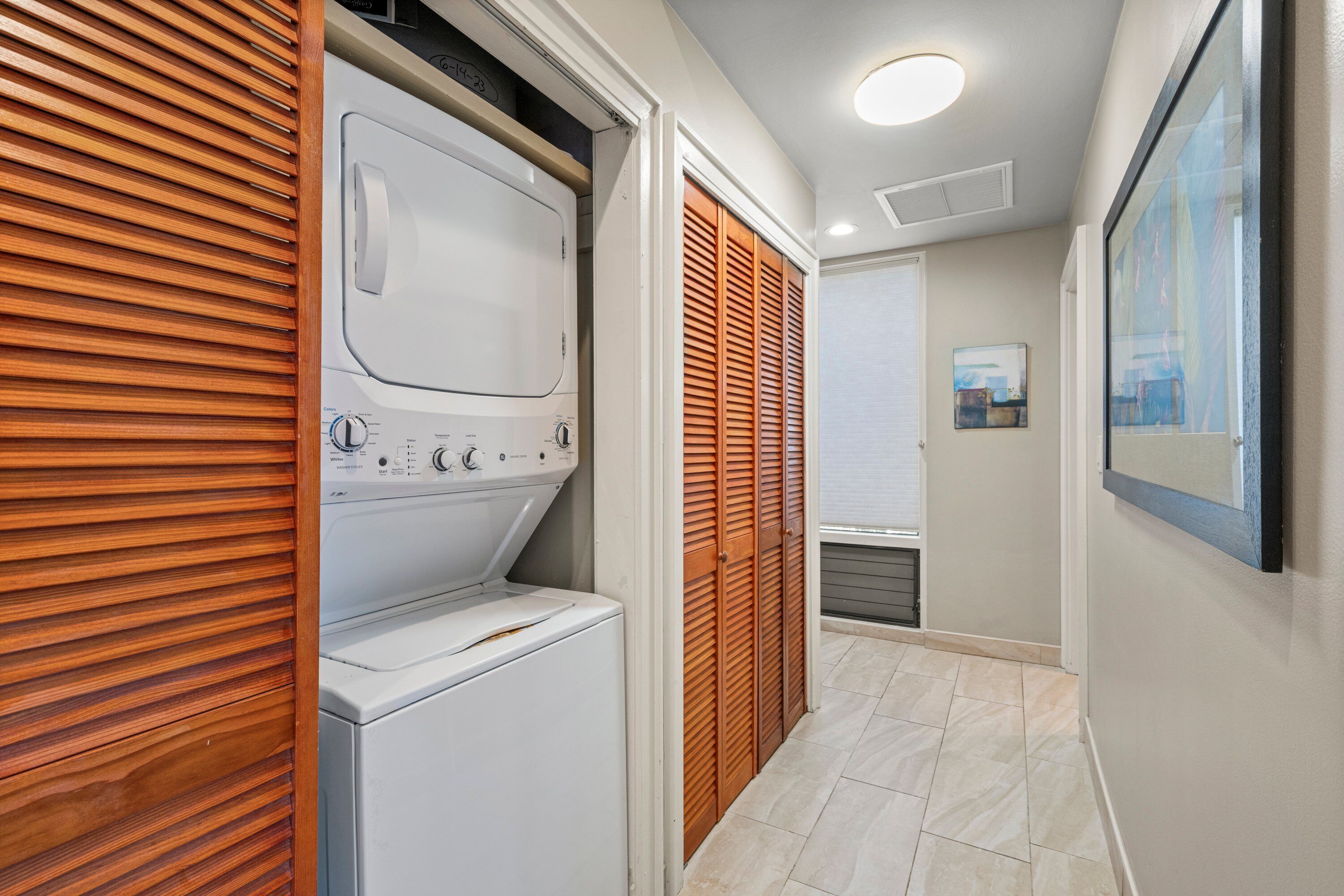 A laundry room with a stacked washer and dryer, wooden sliding doors, and a tiled floor.