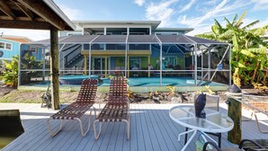 Ein Poolbereich mit zwei Liegestühlen, einem Tisch und einer überdachten Terrasse.