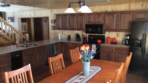A wooden interior with a kitchen featuring dark cabinets, a microwave, and a refrigerator. There is a dining table with chairs and a vase of flowers.