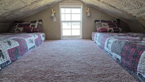 Une chambre mansardée chaleureuse, avec deux lits, une grande fenêtre et un plafond à motifs.