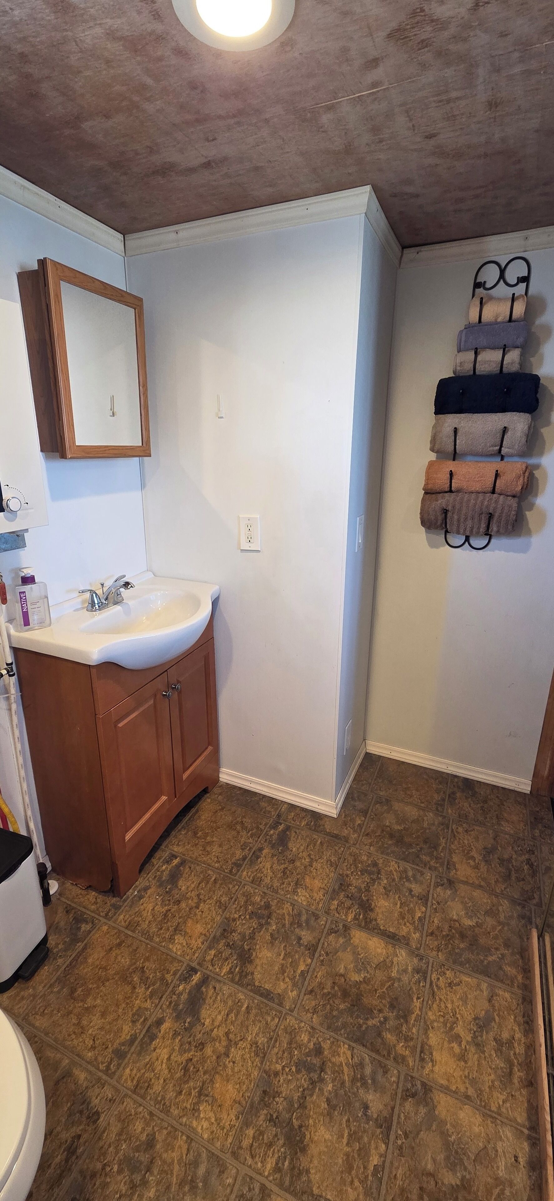 A bathroom with a wooden vanity, a white sink, a mirror, and a towel rack with multiple towels.