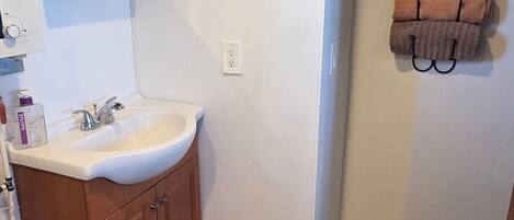 A bathroom with a wooden vanity, a white sink, a mirror, and a towel rack with multiple towels.