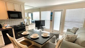Una cocina moderna con armarios blancos, un microondas y una zona de comedor con una mesa negra y sillas blancas.