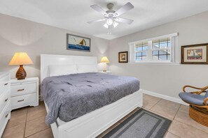 A bedroom with a bed, nightstands, a ceiling fan, a window, and wall art. - Golf Course 6D - Serene golf course villa just steps to the beach and pools! (Miramar Beach)