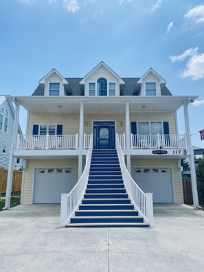 A two-story house with a central staircase leading to a front door, two garage doors, and a balcony on the upper floor. - Private Pool, one block to private beach access and space for everyone (Surf City)