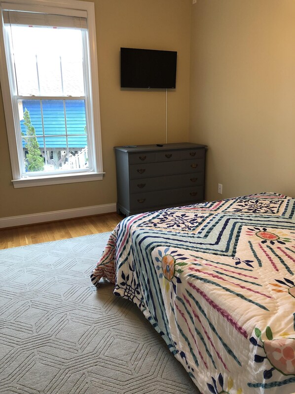 A bedroom with a bed, dresser, and a TV on the wall.