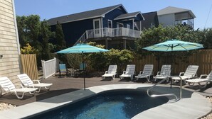 Una piscina con sillas de descanso y sombrillas, rodeada por una terraza de madera y una cerca de madera.