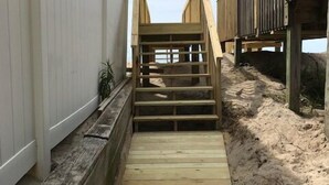 Una escalera de madera que conduce a una zona de playa con un sendero arenoso y una terraza de madera.