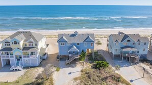 Um imóvel à beira-mar com três casas, cada uma com varanda frontal e pequena varanda. As casas estão adjacentes a uma praia de areia, com o oceano ao fundo.