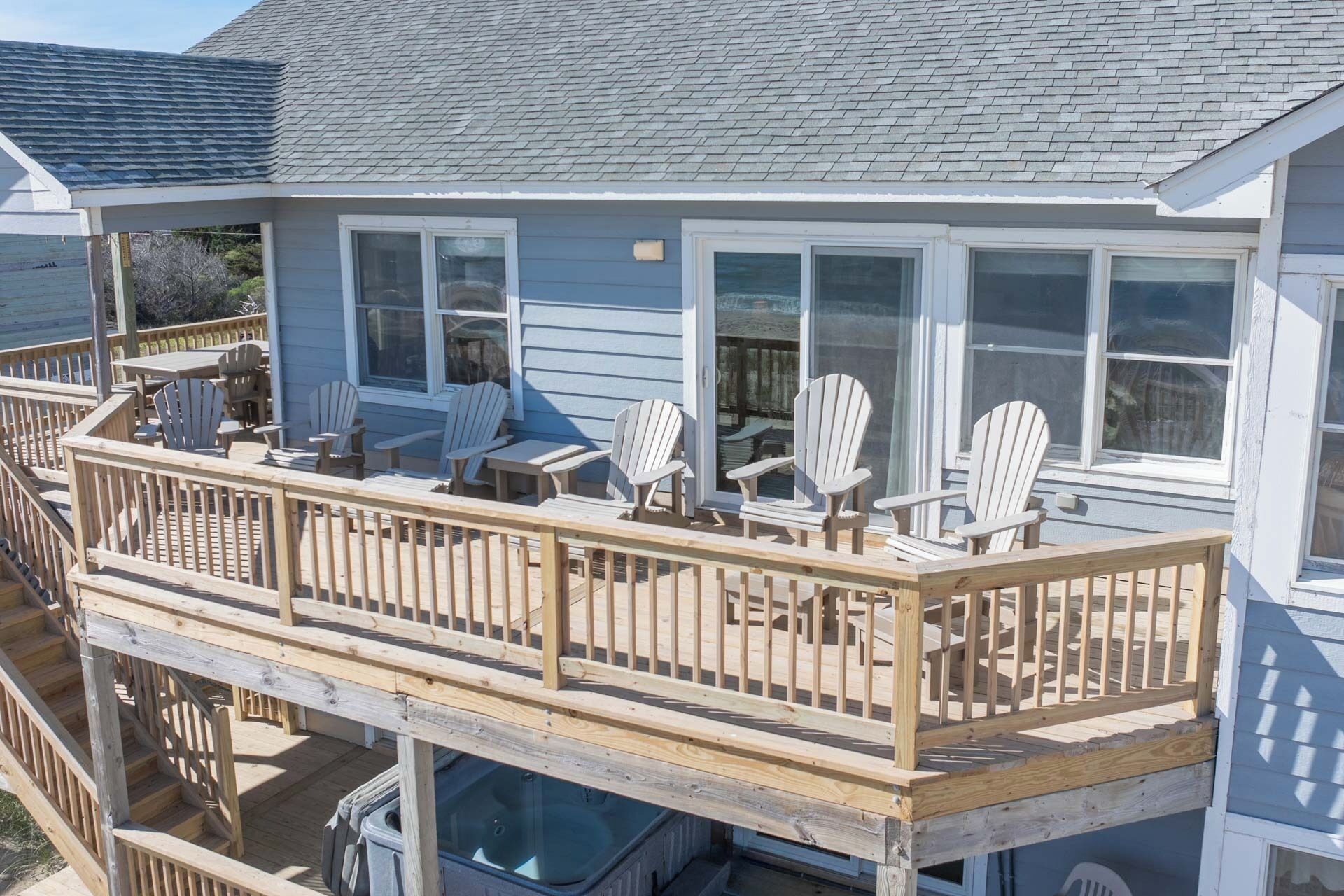 Una casa de dos pisos con balcón, sillones Adirondack y una pequeña mesa.