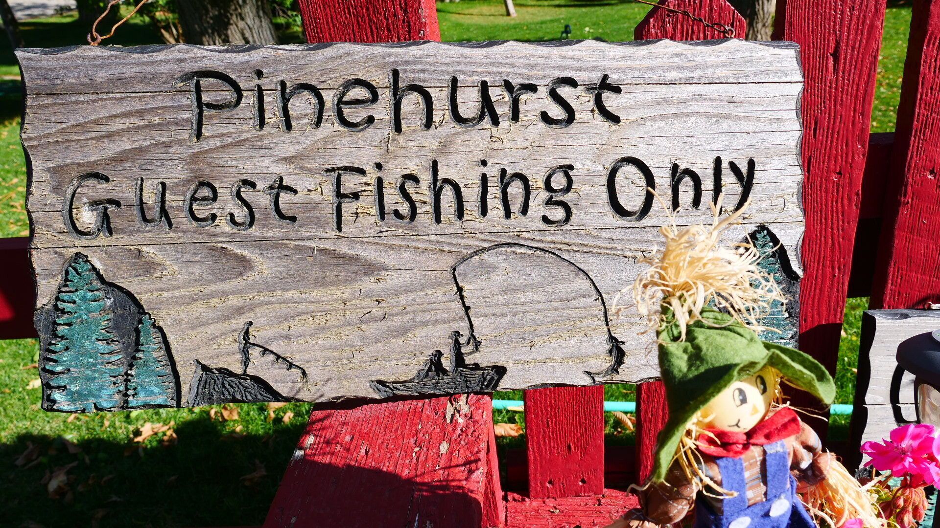 Een houten bord met de tekst 'Pinehurst Guest Fishing Only', bevestigd aan een rode paal met een rustieke uitstraling.