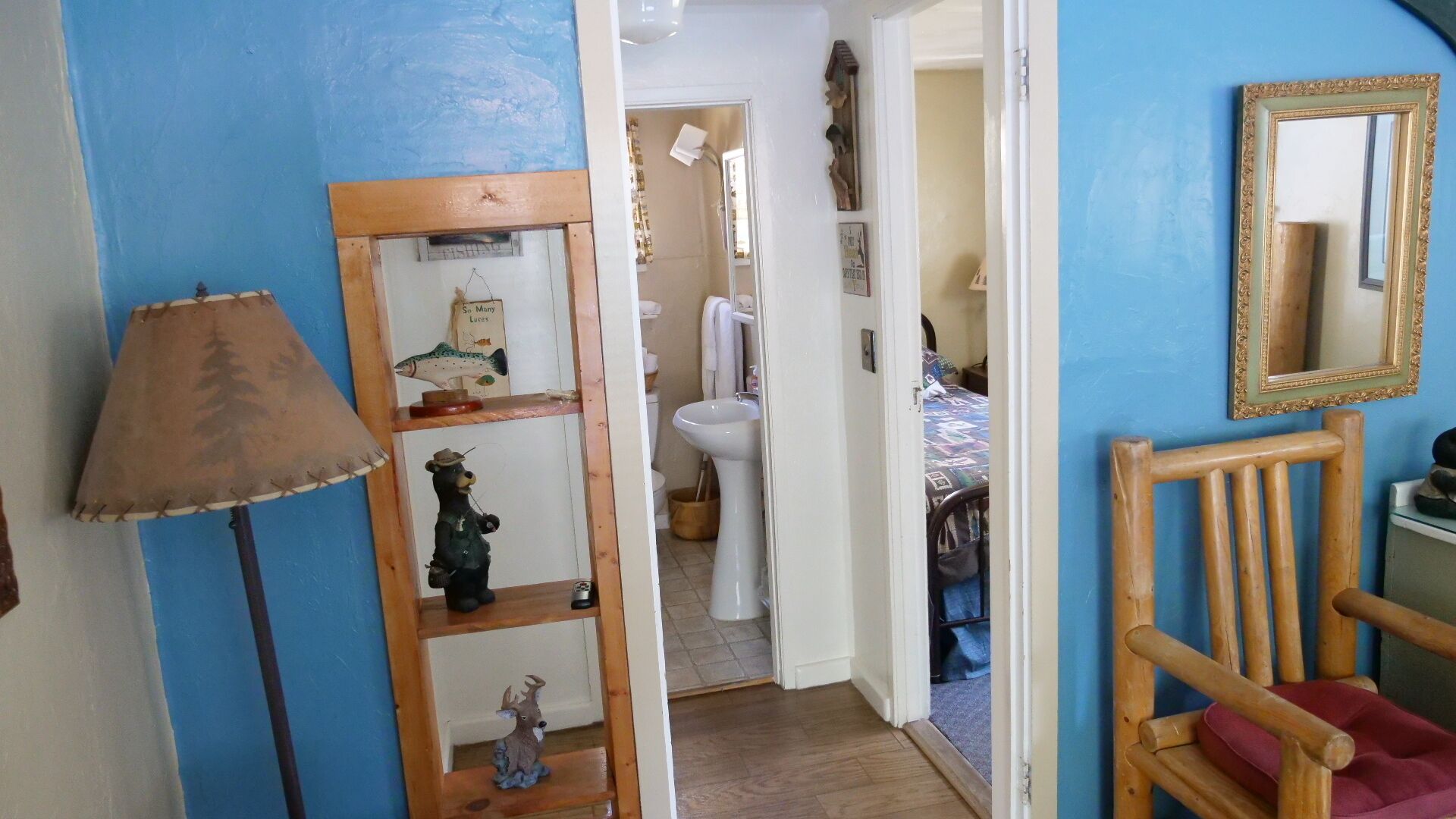 Un couloir avec une lampe, une étagère en bois ornée de figurines de poissons et d’ours, un miroir et une chaise en bois.