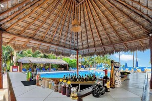 Eine Poolbar mit einem Reetdach, Liegestühlen und Blick auf den Strand.