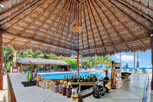 Un espace bar aménagé au bord de la piscine, doté d’un toit de chaume, de chaises longues et offrant une vue sur la plage.