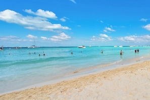 A beach with clear turquoise water, boats, and people swimming.