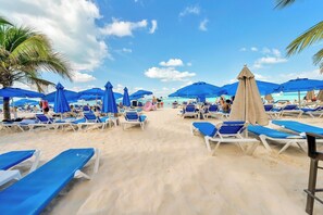 Ein Strand mit Reihen von Liegestühlen und Sonnenschirmen, Palmen und blauem Himmel.