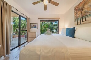 Ein Schlafzimmer mit einem Bett, einem Deckenventilator, einem Fenster mit Blick auf Palmen und einem Gemälde an der Wand.