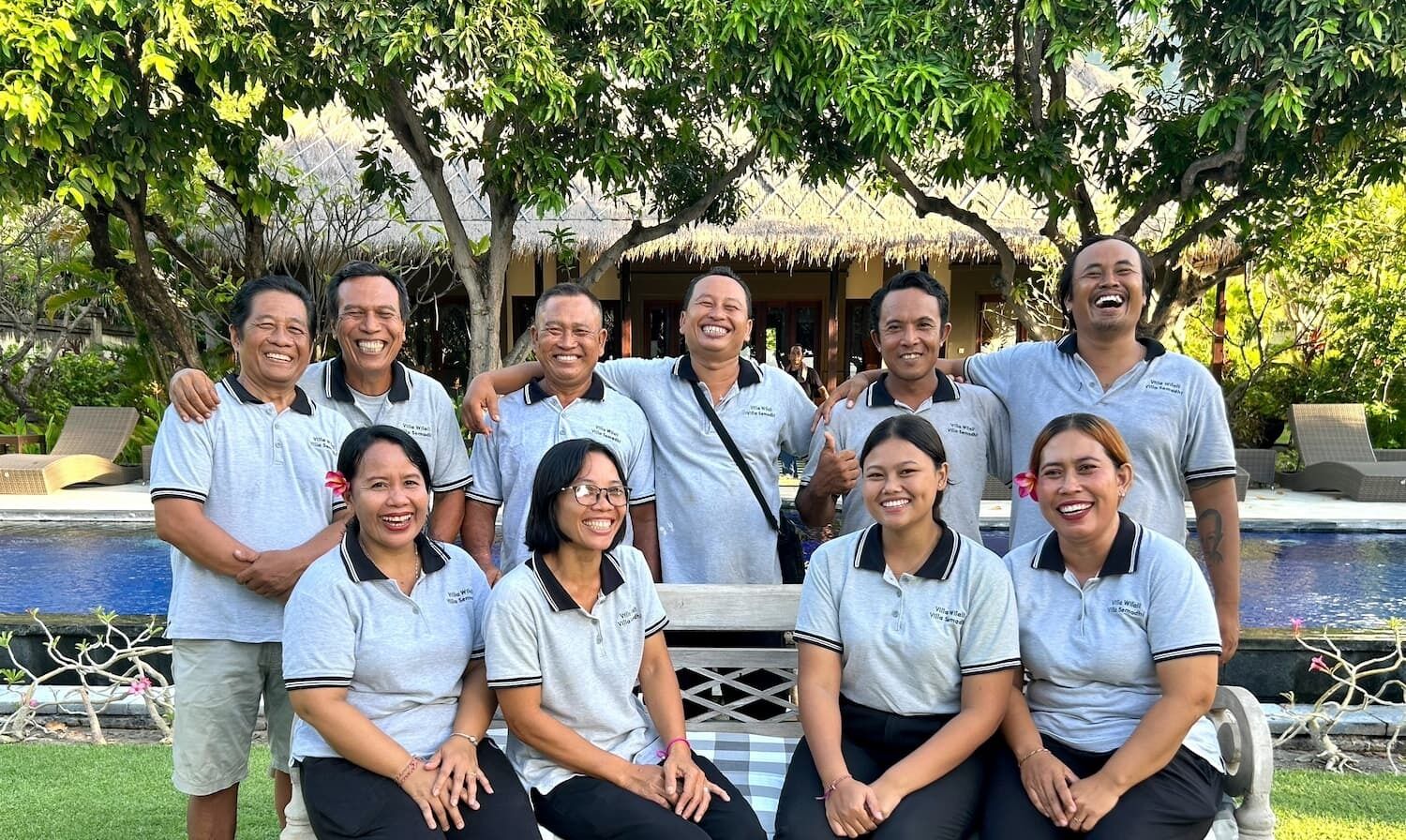 Un grupo de personas en un entorno tropical con una piscina y estructuras de techo de paja al fondo.