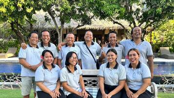Un grupo de personas en un entorno tropical con una piscina y estructuras de techo de paja al fondo.