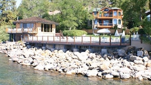 A lakeside lodge with a wooden deck, a small cabin, and a multi-story building with balconies.