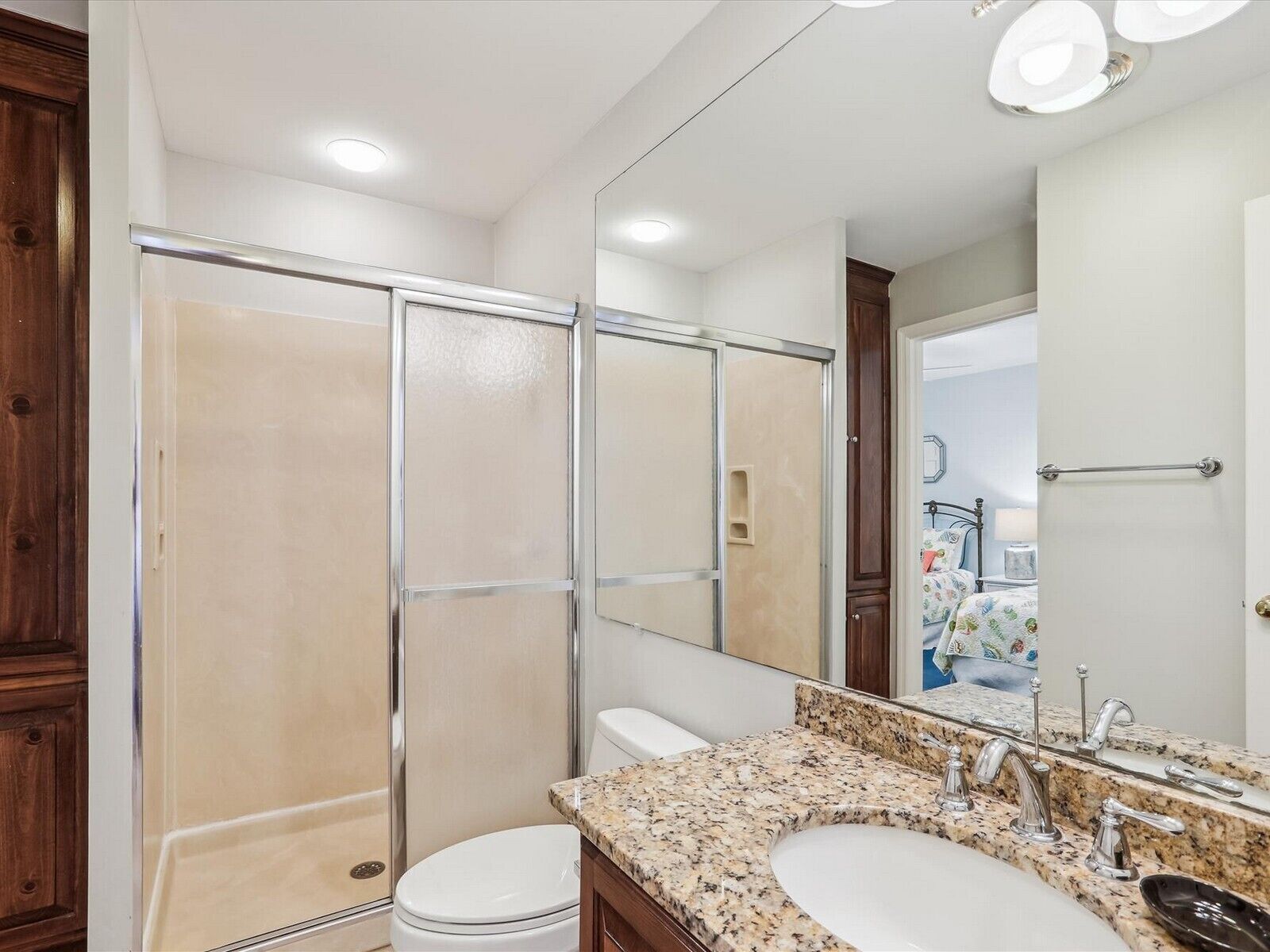 Une salle de bain dotée d’une douche à parois de verre, de toilettes, d’un lavabo avec un plan de travail en granit et d’un grand miroir.