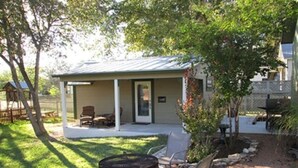 A covered outdoor seating area with a grill and chairs, a small building with a porch, and a fenced yard. - Agape Cottages, Sleeps 9-14, one block to Main Street., 50A EV charging plugs (Fredericksburg)