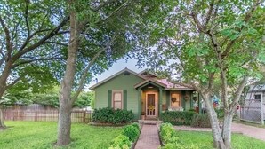 A green house with a front porch, a brick pathway, and a fenced yard. - Agape Cottages, Sleeps 9-14, one block to Main Street., 50A EV charging plugs (Fredericksburg)