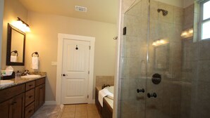 A bathroom with a glass-enclosed shower, a white door, a sink with a mirror, and a towel hanging on the door. - Agape Cottages, Sleeps 9-14, one block to Main Street., 50A EV charging plugs (Fredericksburg)