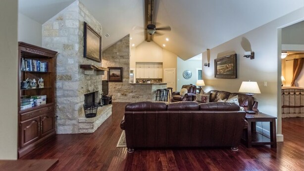 A spacious living room with a stone fireplace, a large leather sofa, and a dining area with a kitchen in the background. - Agape Cottages, Sleeps 9-14, one block to Main Street., 50A EV charging plugs (Fredericksburg)