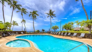 A pool with a curved edge, surrounded by lounge chairs and palm trees. - Nihi Kai 422 Ocean Views, 5 Minute Walk to Beach, Five Stars. Booking Specials! (Koloa)