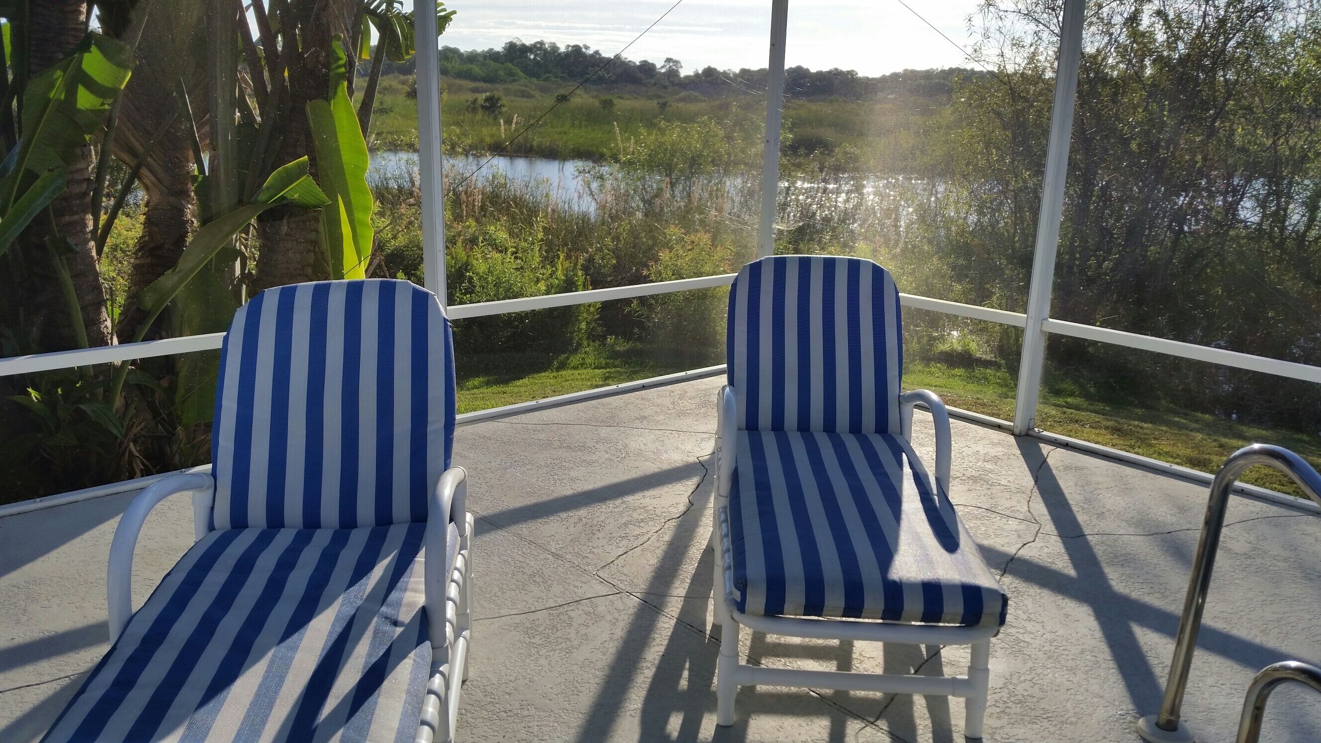 Dos sillones a rayas en un balcón con vistas a un lago y follaje circundante.