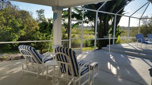 Eine überdachte Terrasse mit weißen Stühlen und einem Tisch, mit Blick auf einen üppigen Garten und Palmen.