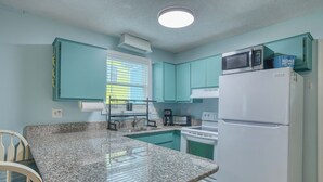 Una cocina con armarios color turquesa, encimera de granito, refrigerador blanco y microondas.