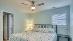 Un dormitorio con cama, ventilador de techo, mesita de noche y ventana con persianas.