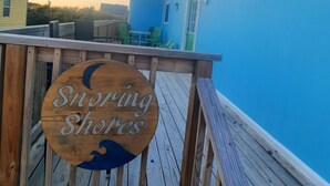 Una terraza de madera con un letrero que dice "Snowing Shores" y una vista de un edificio azul al fondo.