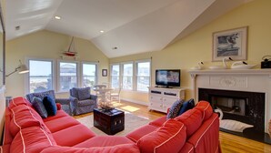 Ein geräumiges Wohnzimmer mit einem großen, roten Sofa, gemusterten Sesseln, einem Kamin und einem Fernseher.