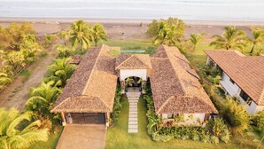 Una propiedad frente a la playa con varios edificios, un camino central y palmeras.