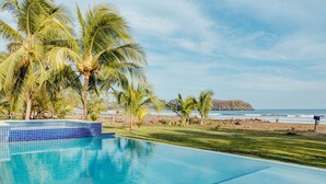 Una piscina azul cristalina con borde de azulejos, rodeada de palmeras y vista al océano.
