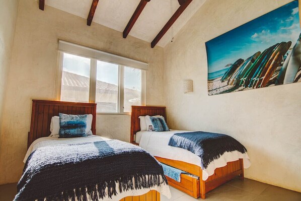 Ein Schlafzimmer mit zwei Holzbetten, einem großen Fenster und einem Strandbild an der Wand.