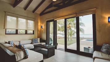 Relax in this spacious living area with a high ceiling and comfortable seating, offering a view of the pool and palm tree through large sliding glass doors.