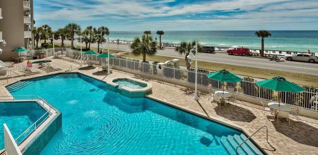 Una piscina con idromassaggio, circondata da lettini e ombrelloni, con vista su una spiaggia e l'oceano.