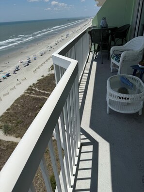 A balcony with a view of the beach, wicker furniture, and a table.