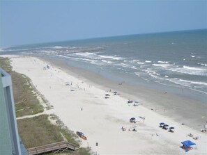A beach with a pier in the distance, sandy shore, and people enjoying the beach. - Awesome Oceanfront Condo, Unique Custom Features, Paradise Pointe, Cherry Grove (North Myrtle Beach)